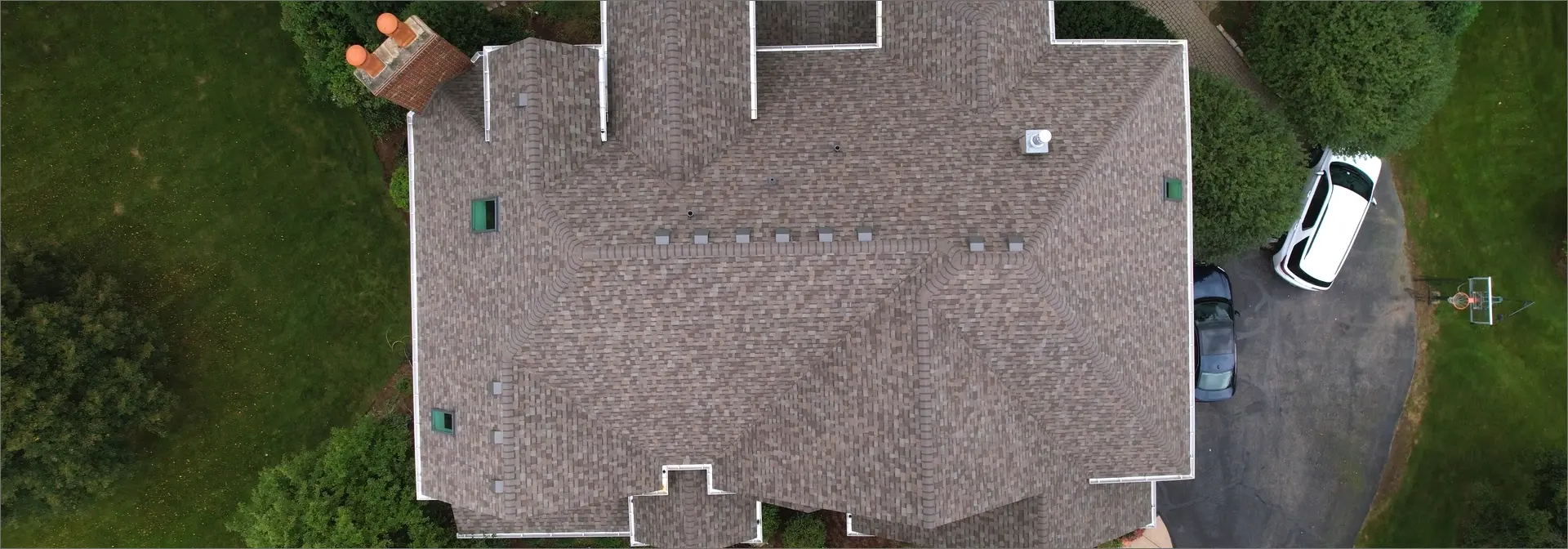 Overhead view of a home with a recently replaced roof by 3JM Exteriors. Right side of the home has 2 cars parked in driveway near a basketball hoop. 